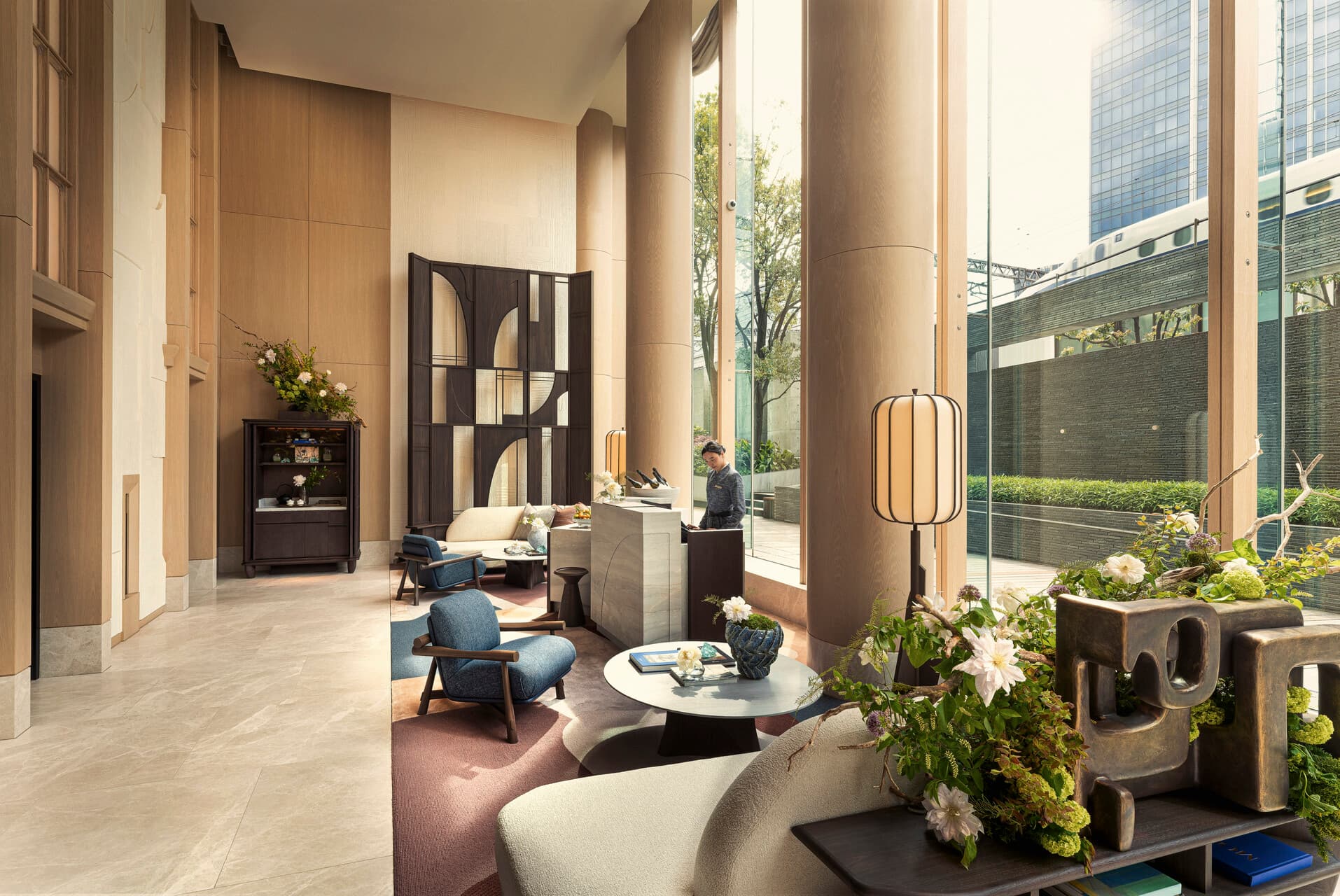 Four Seasons Hotel Tokyo at Marunouchi lobby with oak columns, navy lounge chairs, and a shinkansen passing beyond the glass
