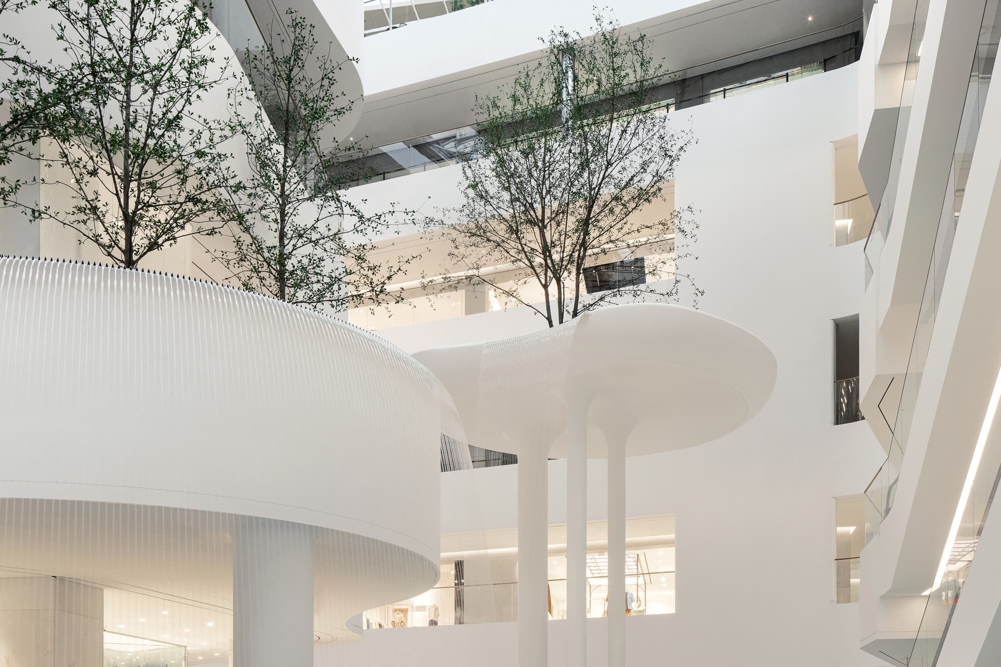 White biomorphic islands, trees, and water curtain of the Waterfall Garden atrium at The Hyundai Seoul, Yeouido