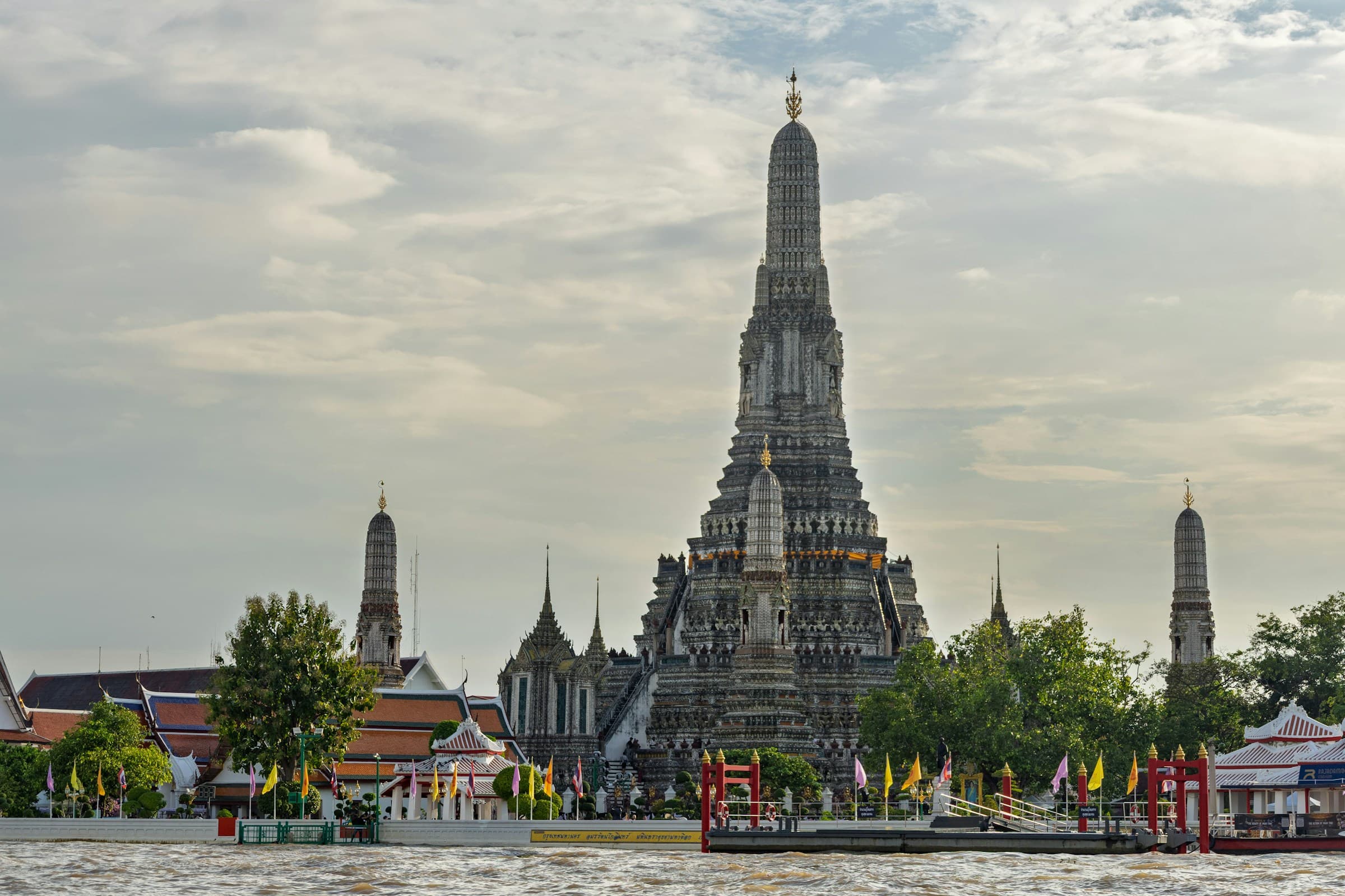 Wat Arun from the Chao Phraya, the central prang and riverside flags in daylight