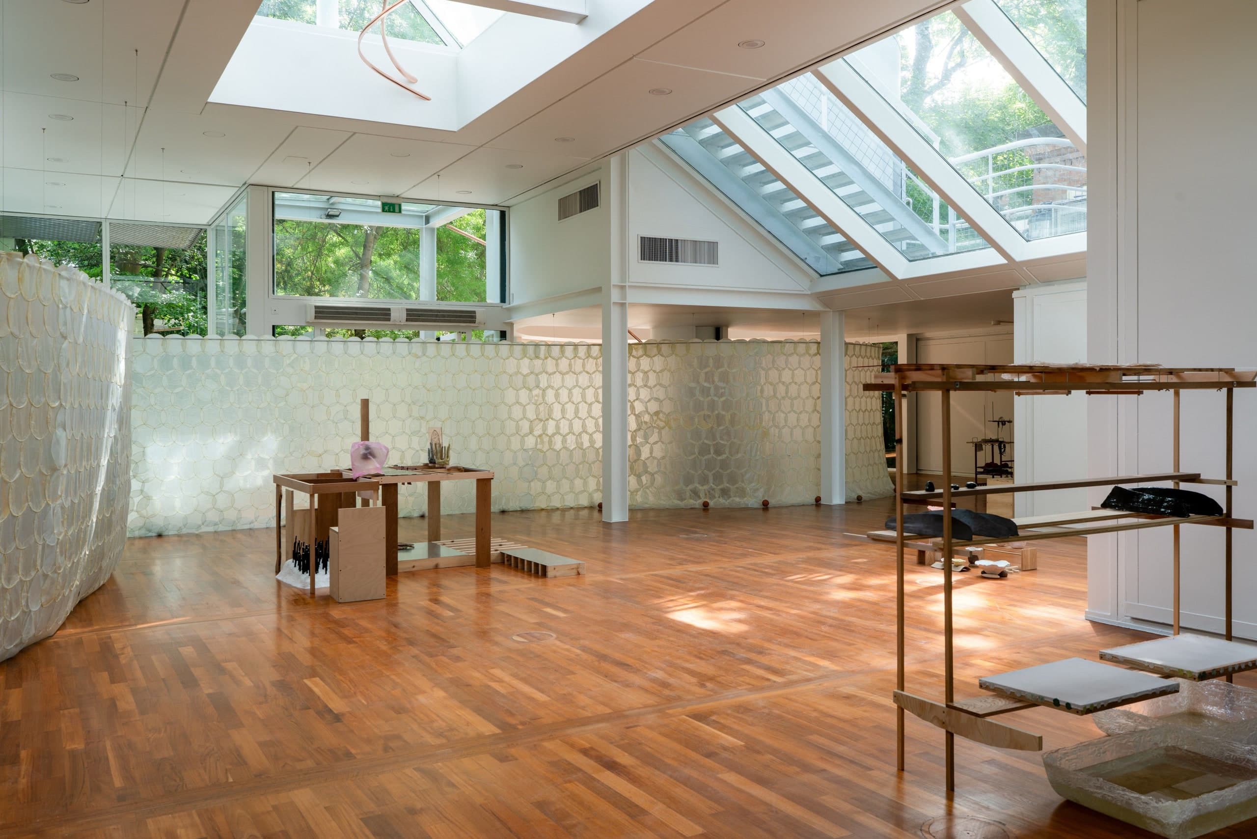Korean Pavilion interior at the Giardini, Venice, with wood floors, skylight, and park trees beyond the glass