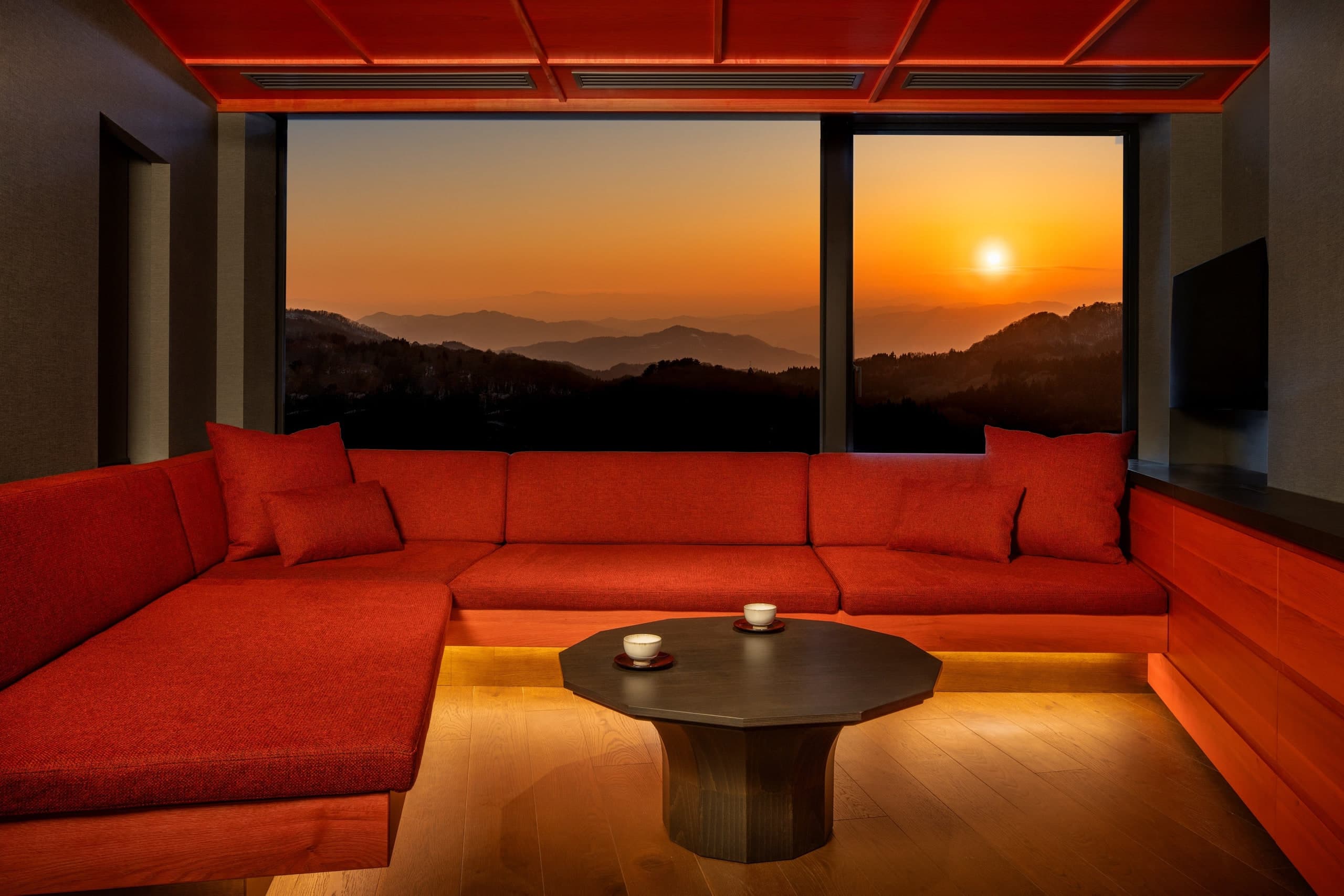 Crimson Modern guest room at KAI Zao with a red sectional sofa, panoramic mountain window, and warm wood cabinetry
