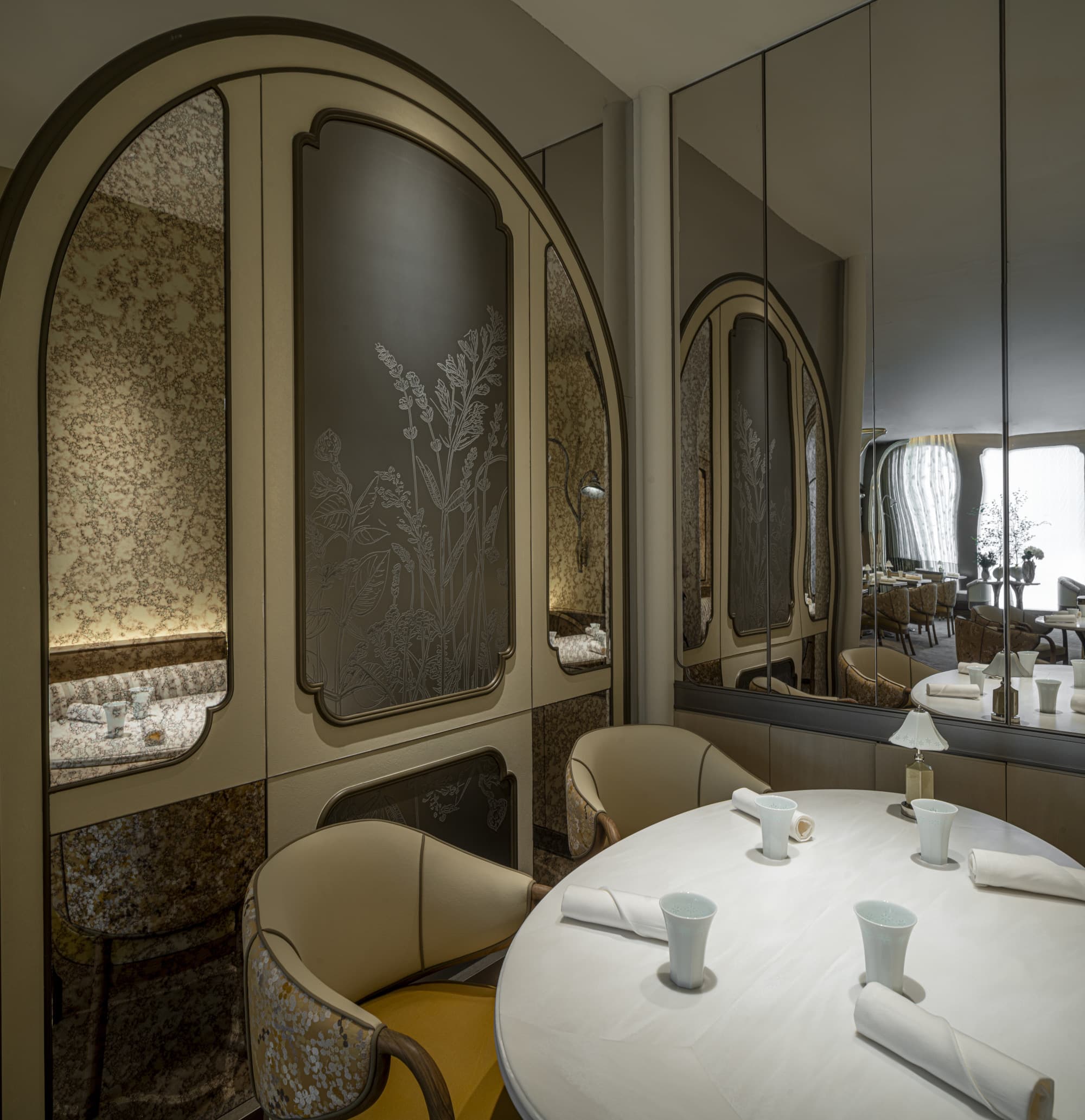 Round Tate table for four with embroidered chair backs, pale ceramic cups, and mirrored wall reflecting the Sheung Wan dining room