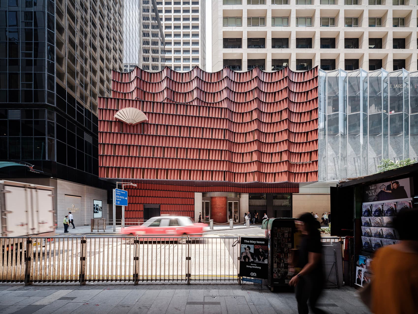 Terracotta undulating facade of Mandarin Oriental The Landmark on Queen's Road Central with the gold fan logo and a Hong Kong taxi passing