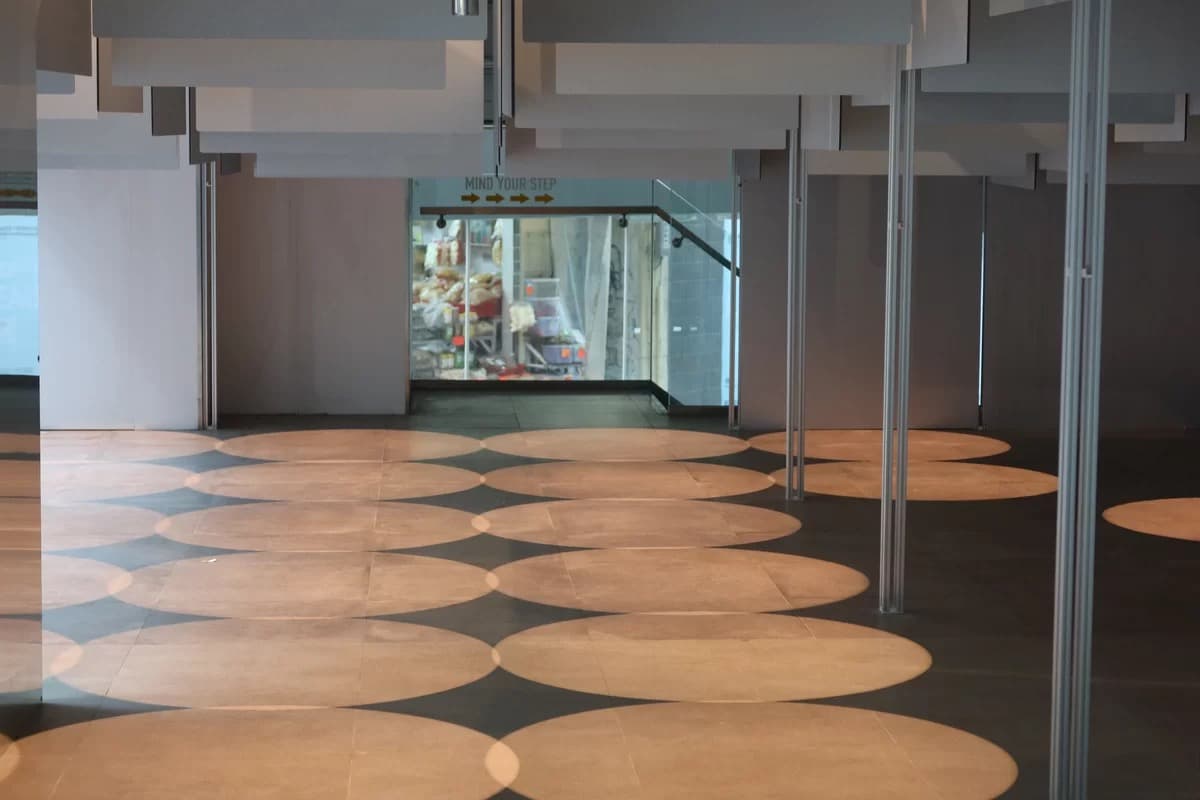 Infinite Maze 189 interior at PROJCT with circular floor grid, hanging ceiling panels, and Queen’s Road West shops beyond the glass