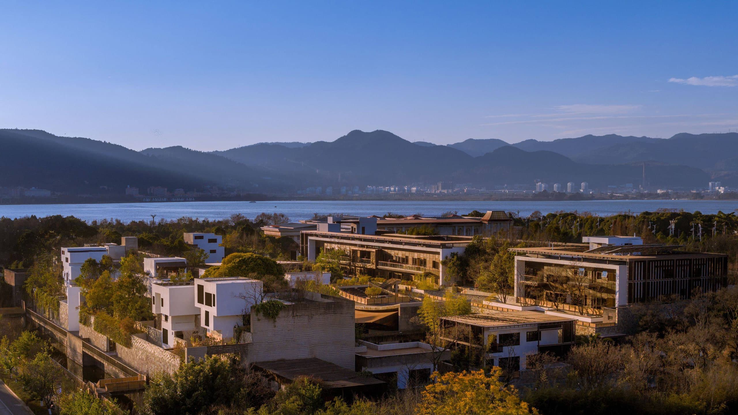 Songtsam Linka Kunming terraced white and timber buildings on a wooded hillside overlooking Dianchi Lake and distant mountains