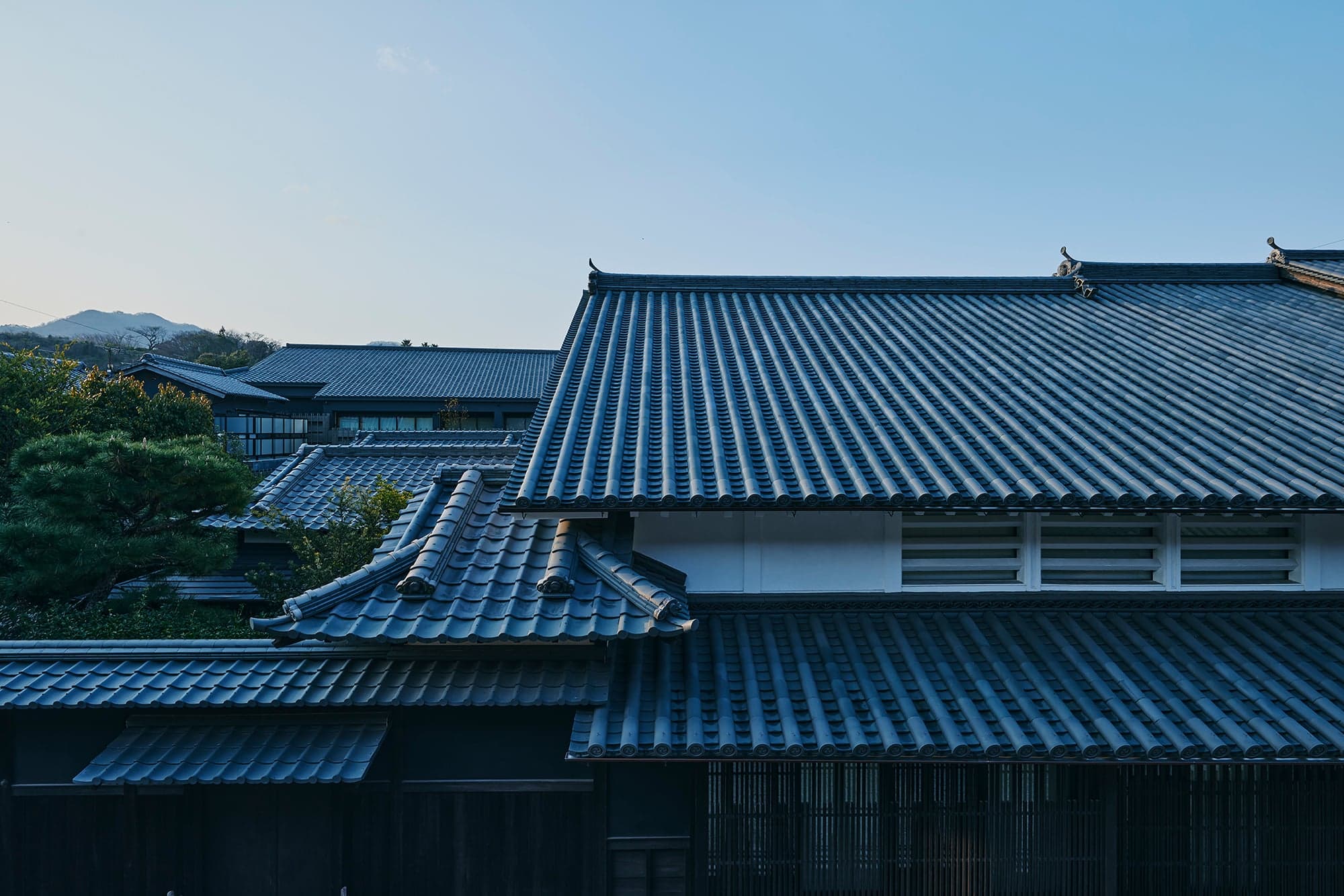 Overlapping dark-tiled roofs of Azumi Setoda against a pale Setouchi sky on Ikuchijima
