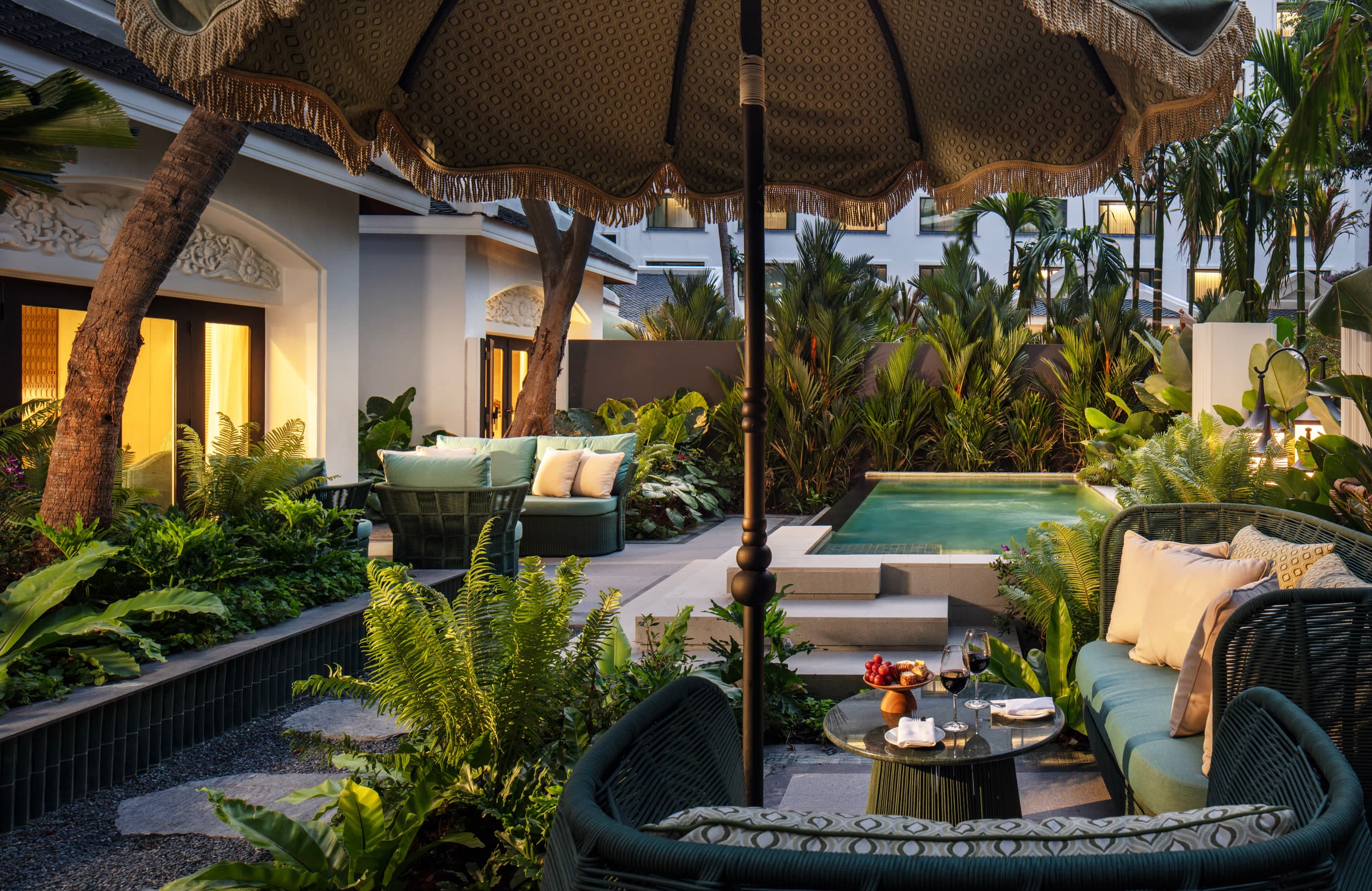 A private pool in a planted courtyard at dusk, with a fringed umbrella and wicker sofas at Anantara Siam Bangkok