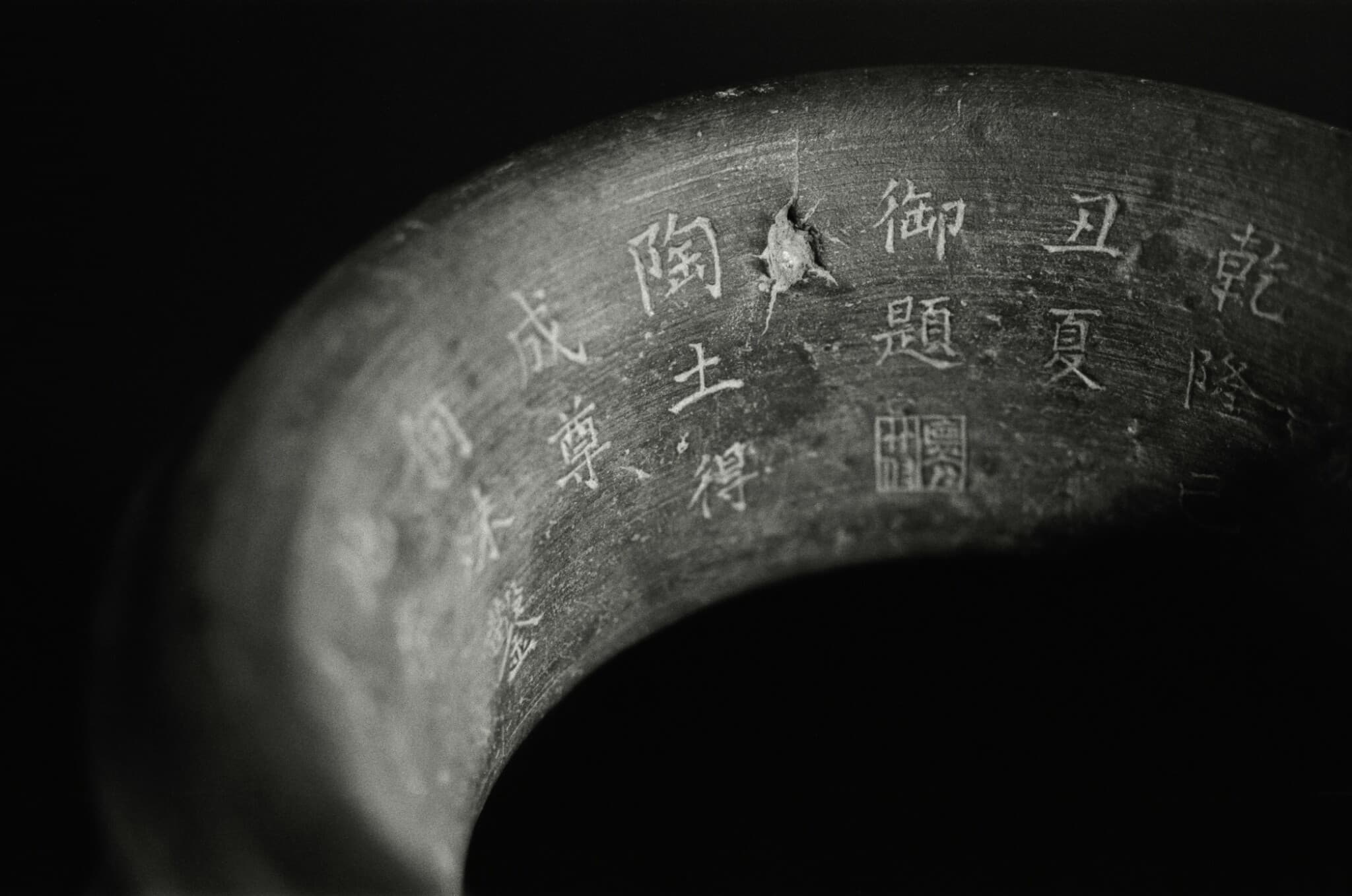 Close view of an incised Chinese inscription and a small loss on the dark rim of a pottery jar