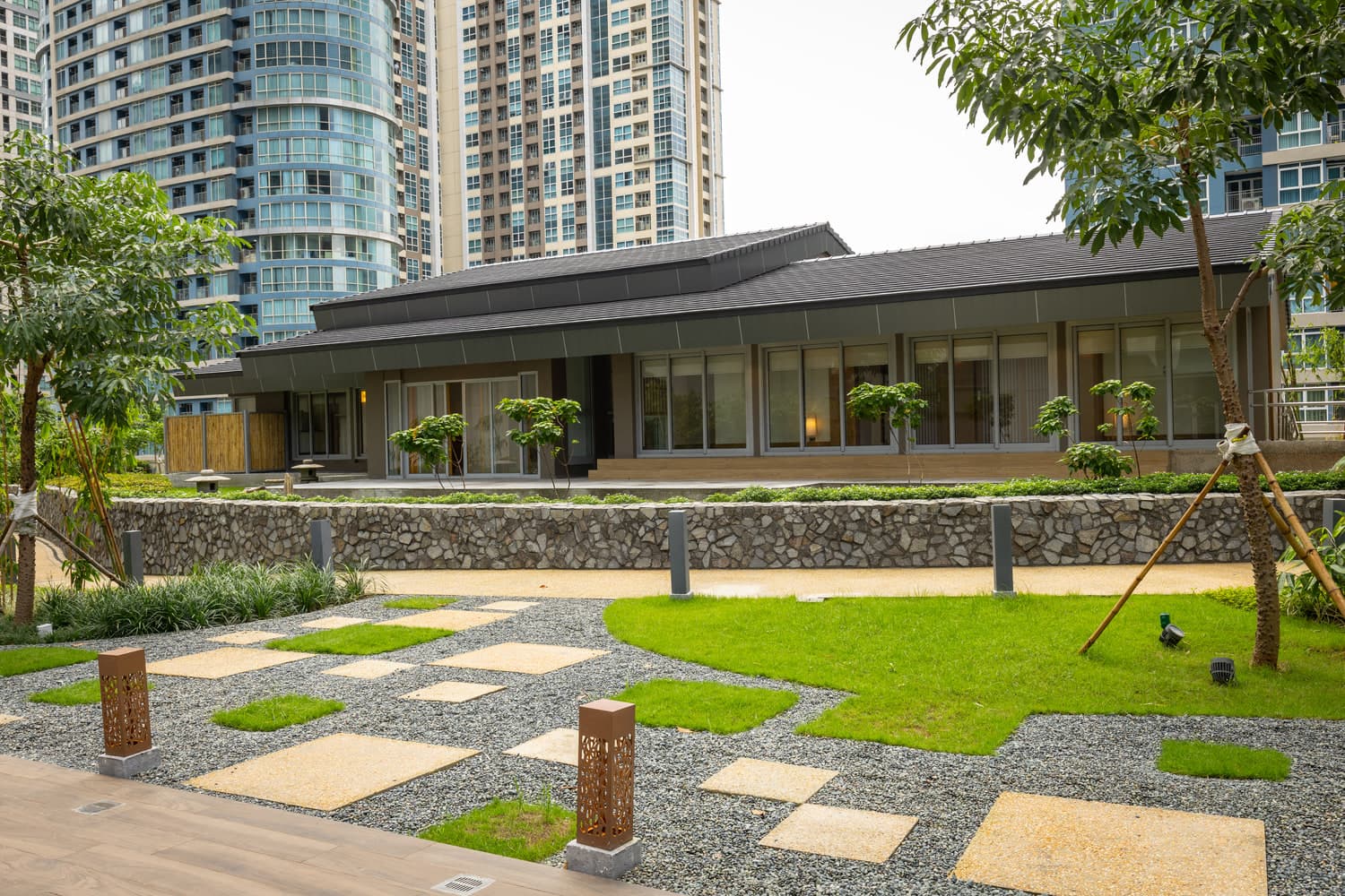 Single-storey Guest House pavilion with a dark hip roof beside a gravel garden and stepping stones, residential towers behind, at The Seasons Residences in Bonifacio Global City