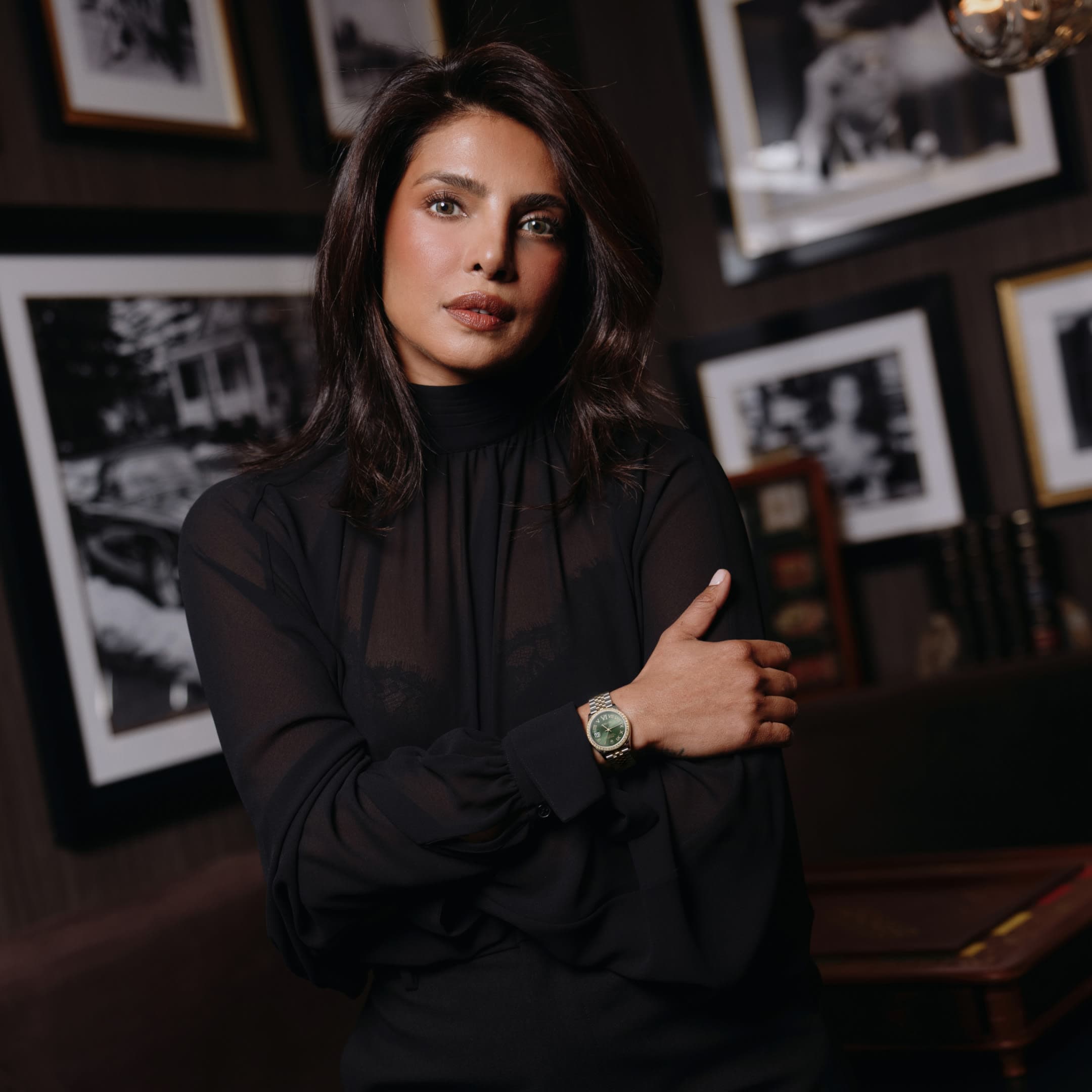 Priyanka Chopra Jonas in a black sheer turtleneck with arms crossed, wearing a Rolesor Datejust with olive green dial, fluted bezel, and Jubilee bracelet
