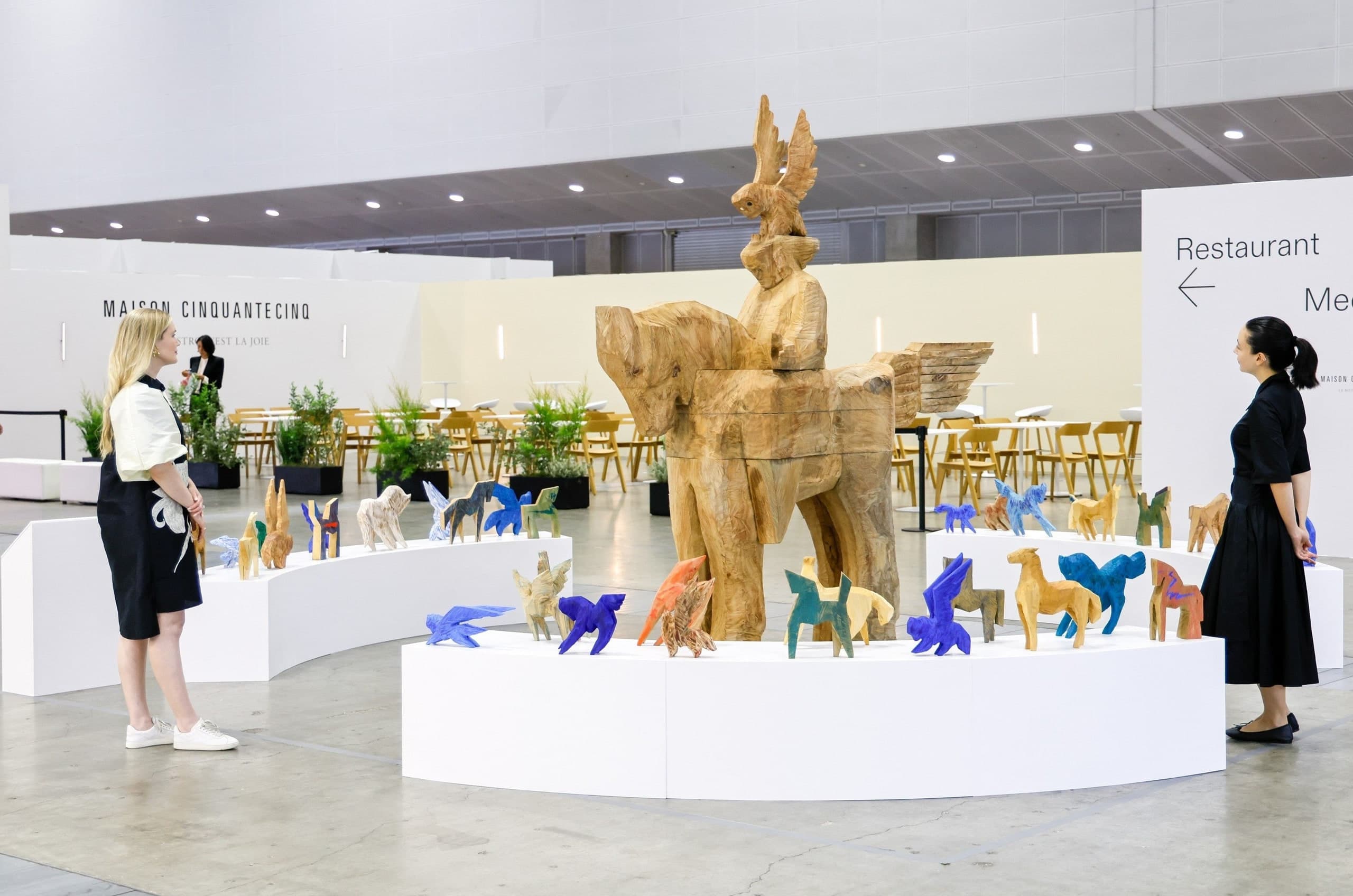 Visitors viewing Marco Gallery's wooden rider-and-horse installation beside the Maison Cinquantecinq dining lounge at Tokyo Gendai, PACIFICO Yokohama