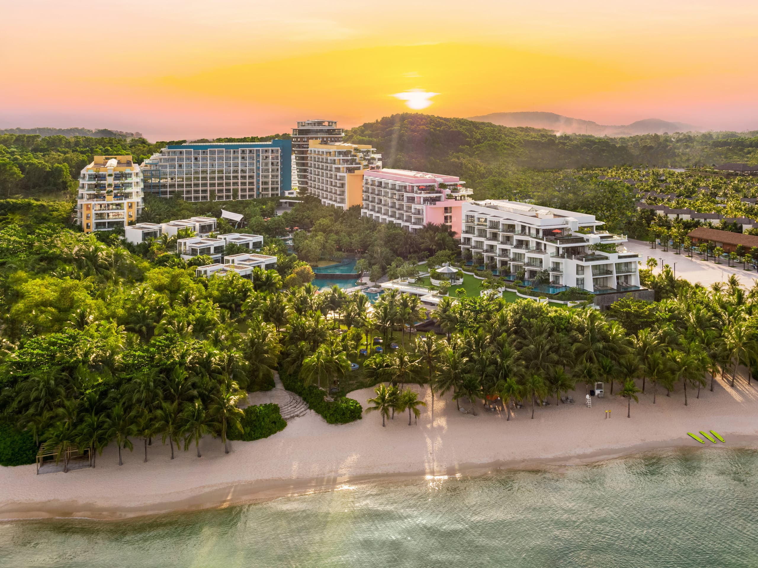 Aerial view of Premier Residences Phu Quoc Emerald Bay along Kem Beach at sunset, with hotel towers and villa residences set in tropical forest