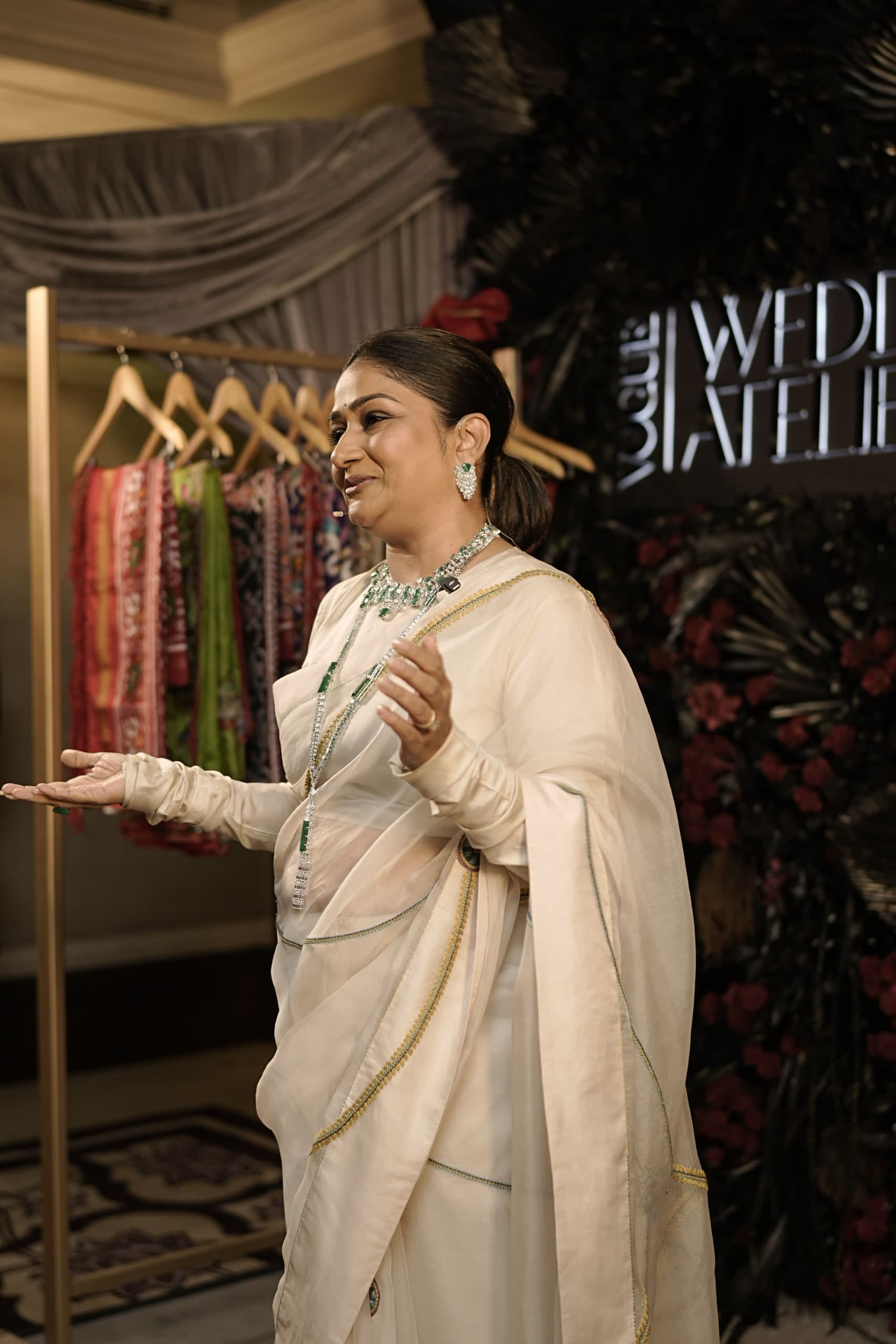 Speaker in embroidered sari and emerald jewelry beside a couture rack and Vogue Wedding Atelier signage at Taj Palace, New Delhi