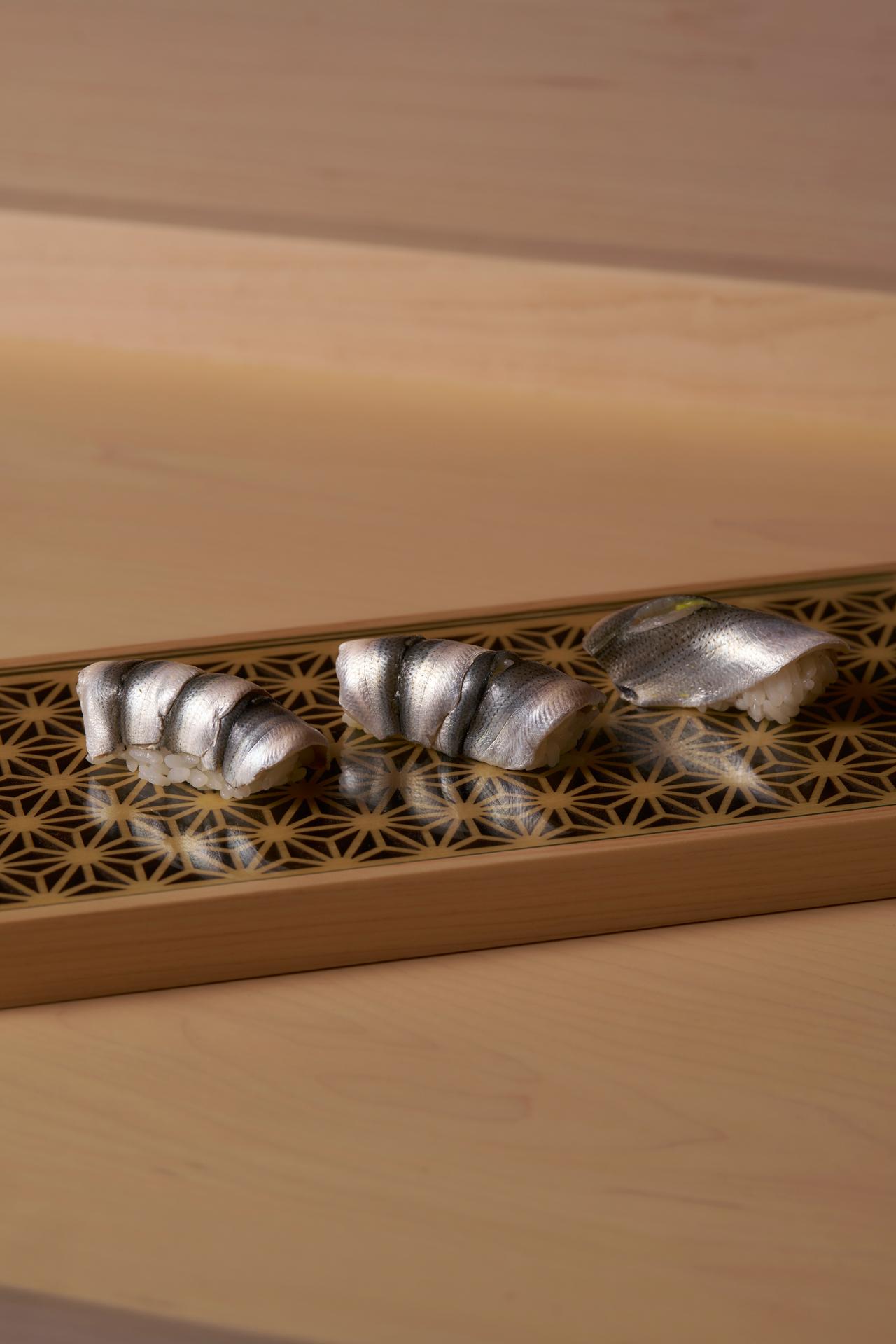 Three pieces of shinko nigiri on a wooden board inlaid with a kumiko lattice
