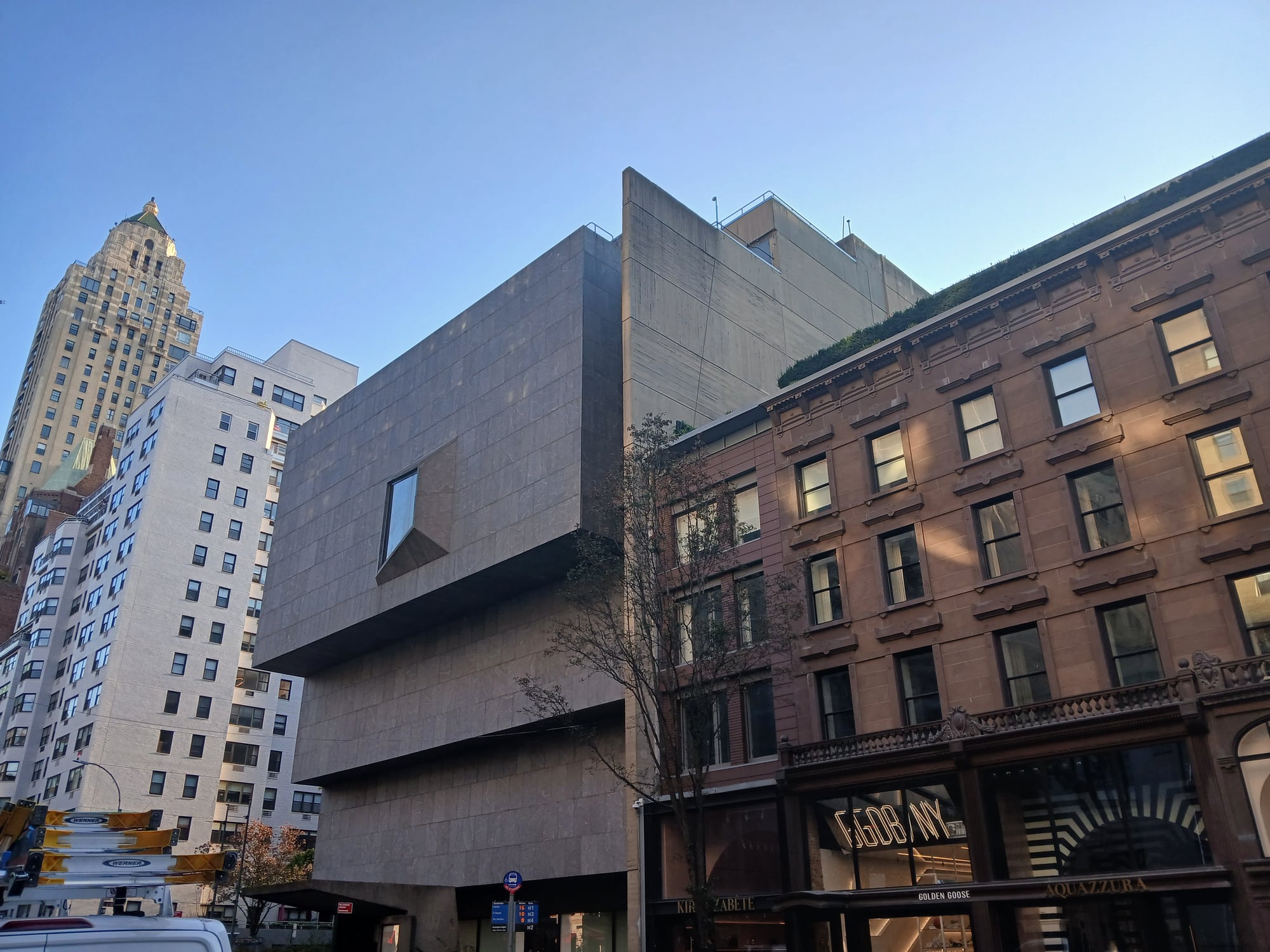 Breuer building on Madison Avenue with neighboring brownstone retail and Carlyle Hotel roof beyond
