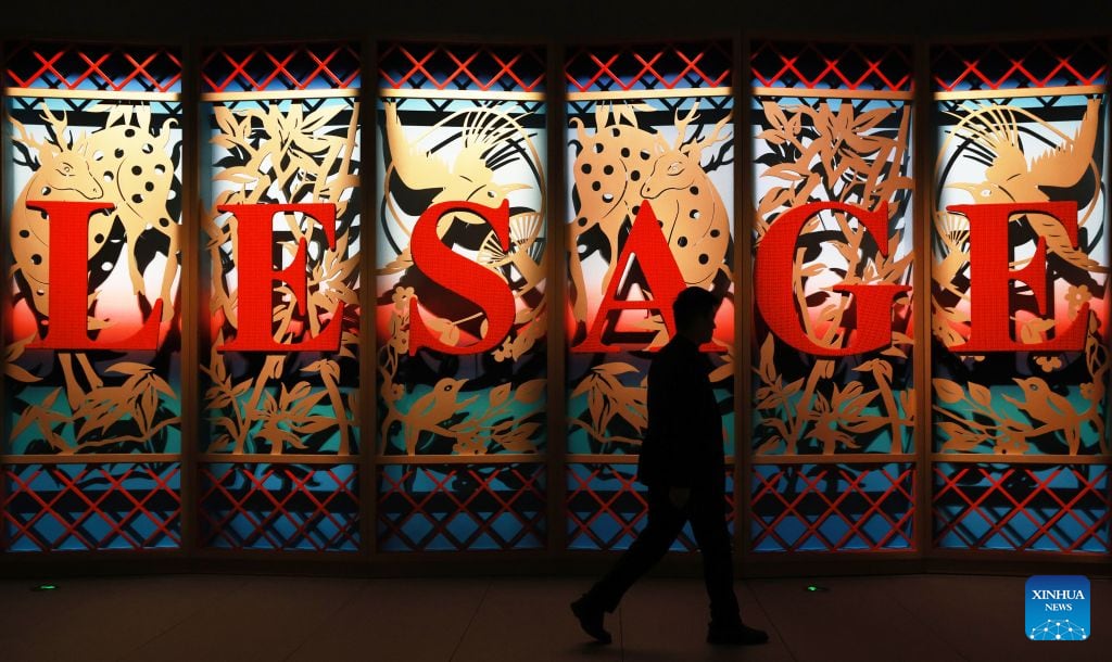 A visitor walks past a red LESAGE sign set into a gold bird-and-flower screen