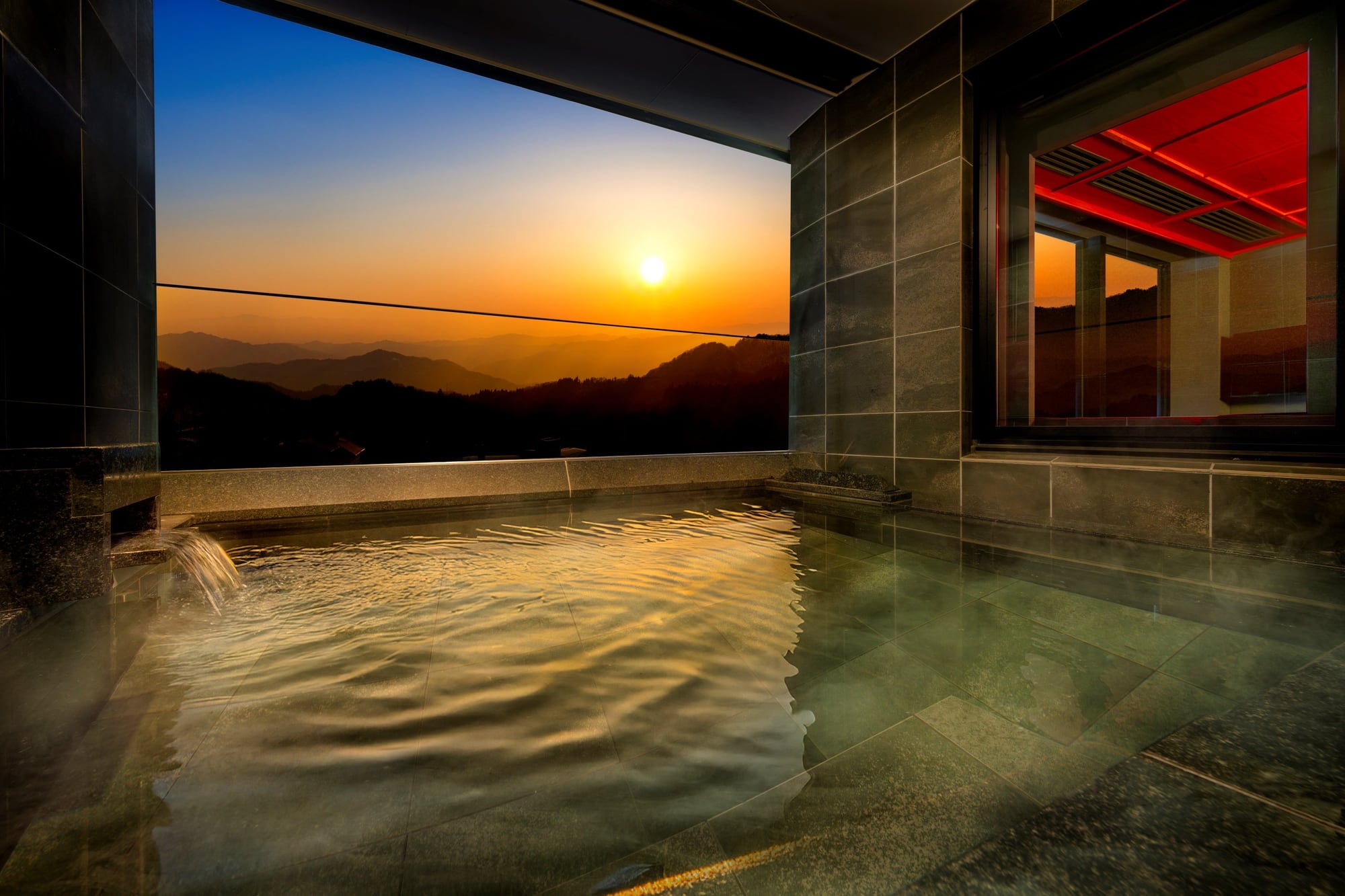 Private outdoor stone bath on a KAI Zao guest-room terrace overlooking the Zao mountain range at sunset