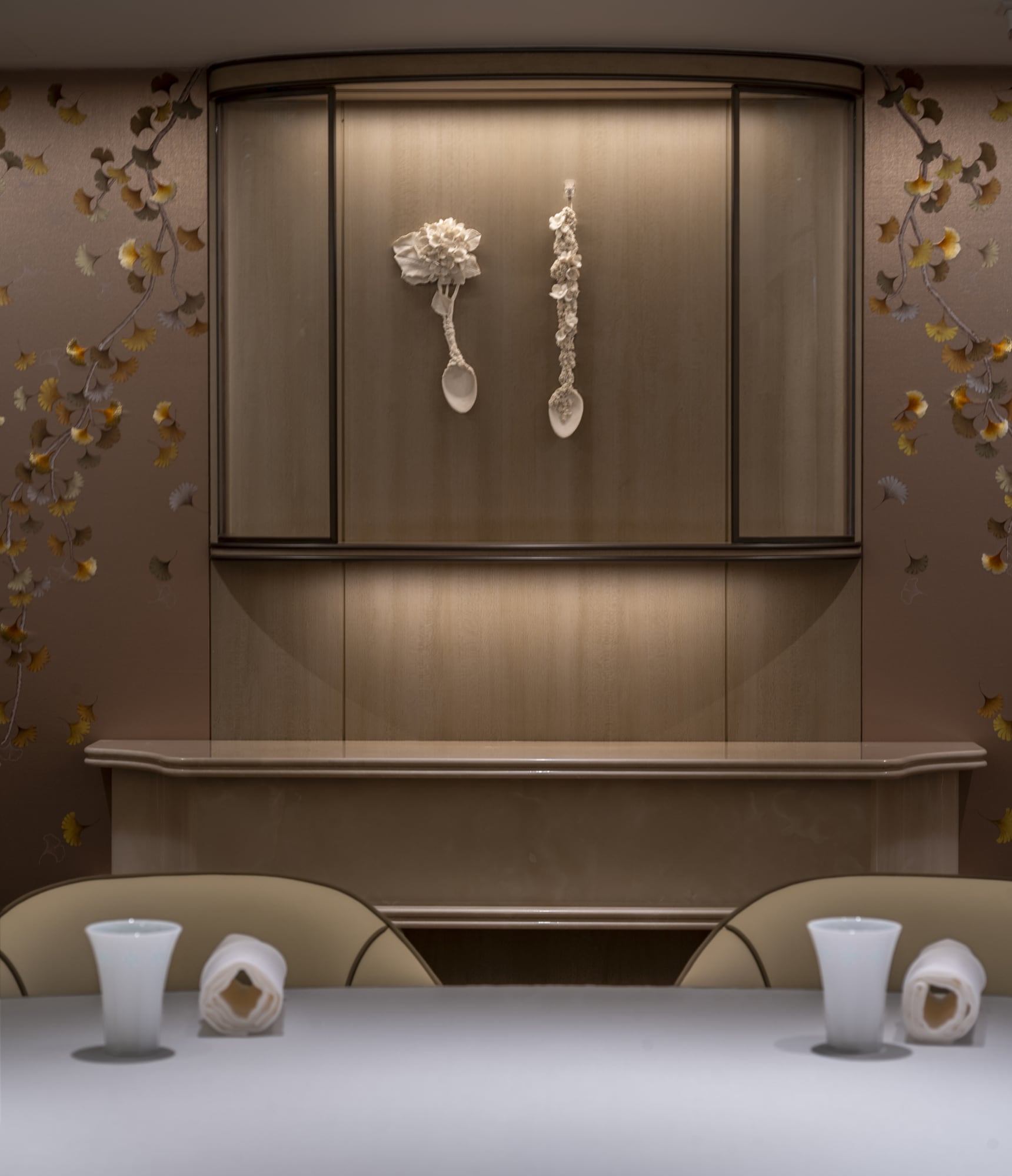 Two floral porcelain spoons displayed in a lit wood niche above a Tate place setting