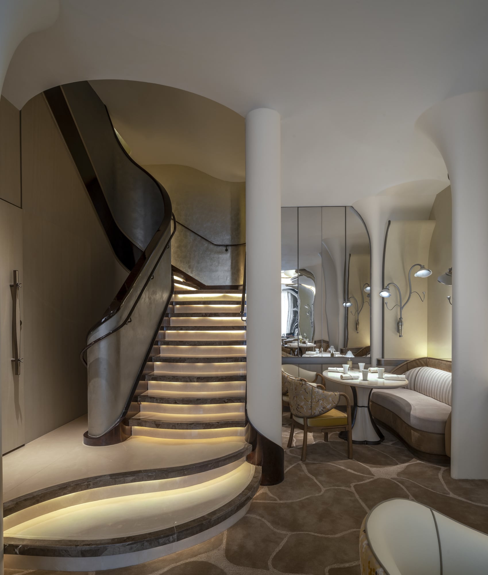 Lit curved staircase beside a two-seat dining nook at Tate