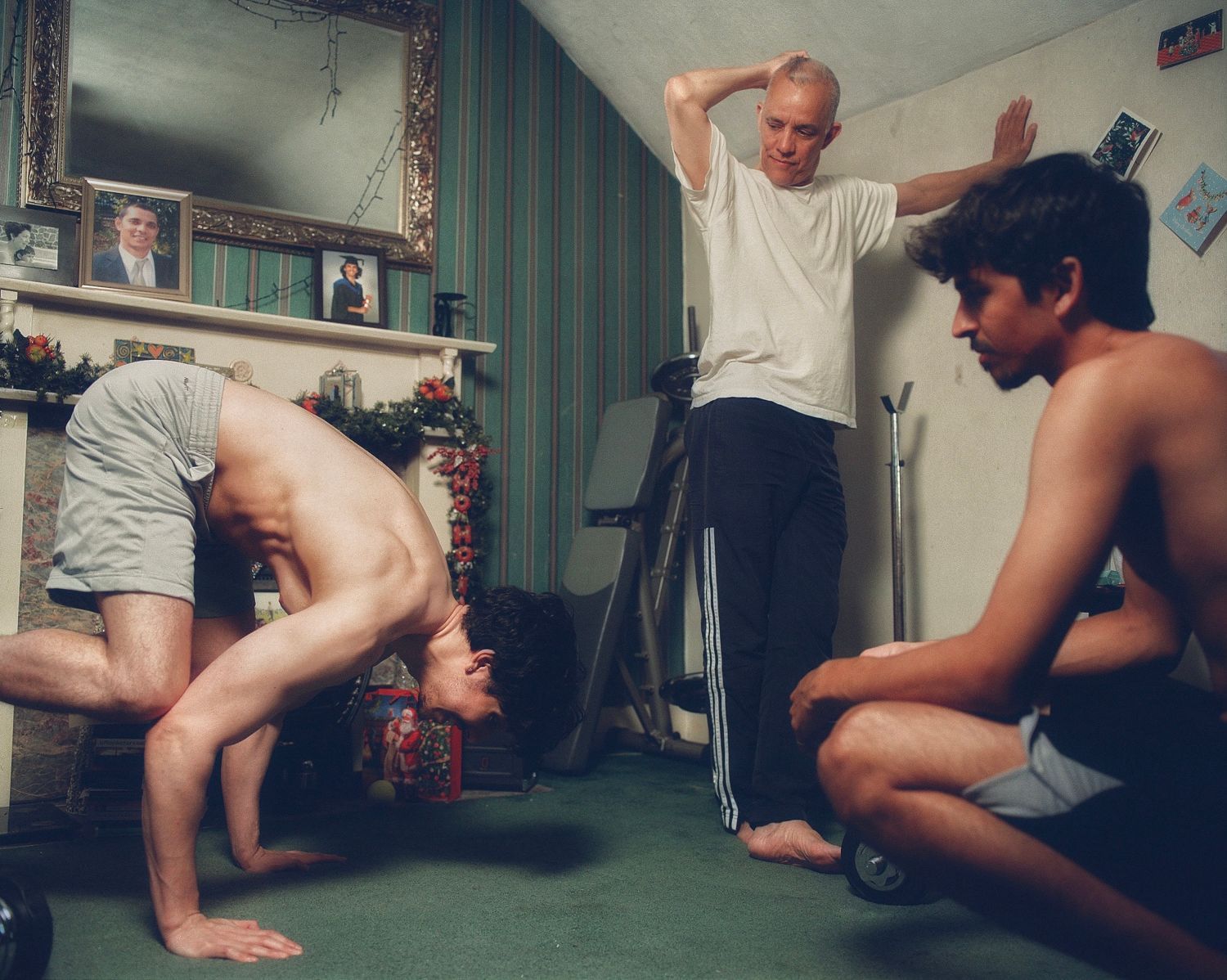 Three men in a domestic room with exercise gear from Adam Han-Chun Lin’s Sonder series