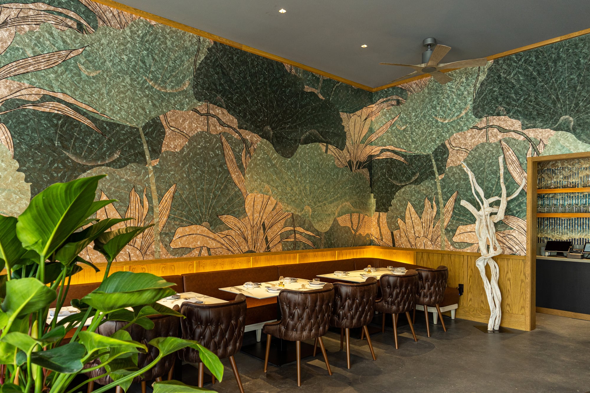 Banquette seating under a lotus mural at Kingfisher with tufted leather chairs