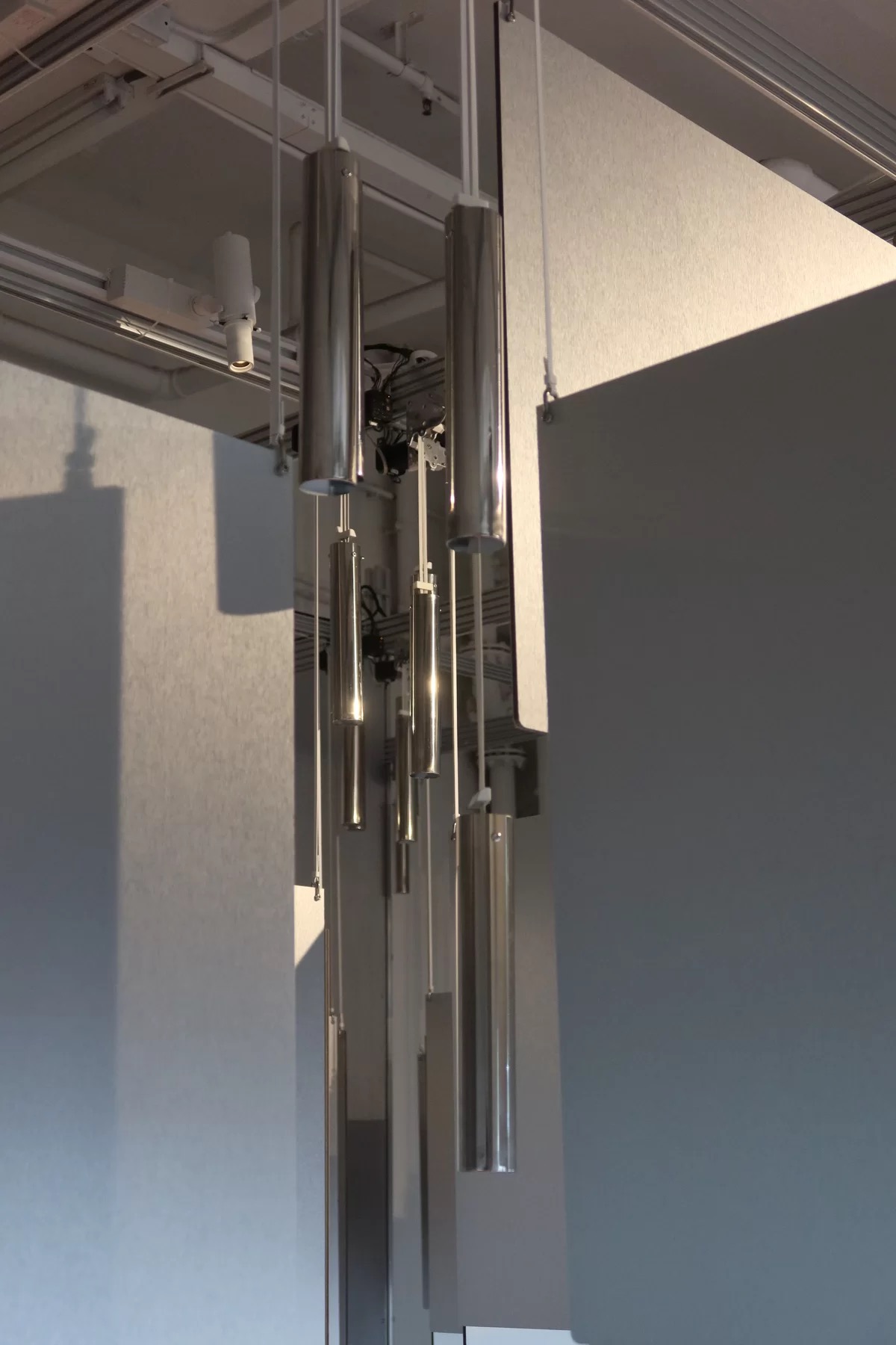 Chrome cylinders hung on cords between pale vertical panels inside Infinite Maze 189 at PROJCT Sai Ying Pun