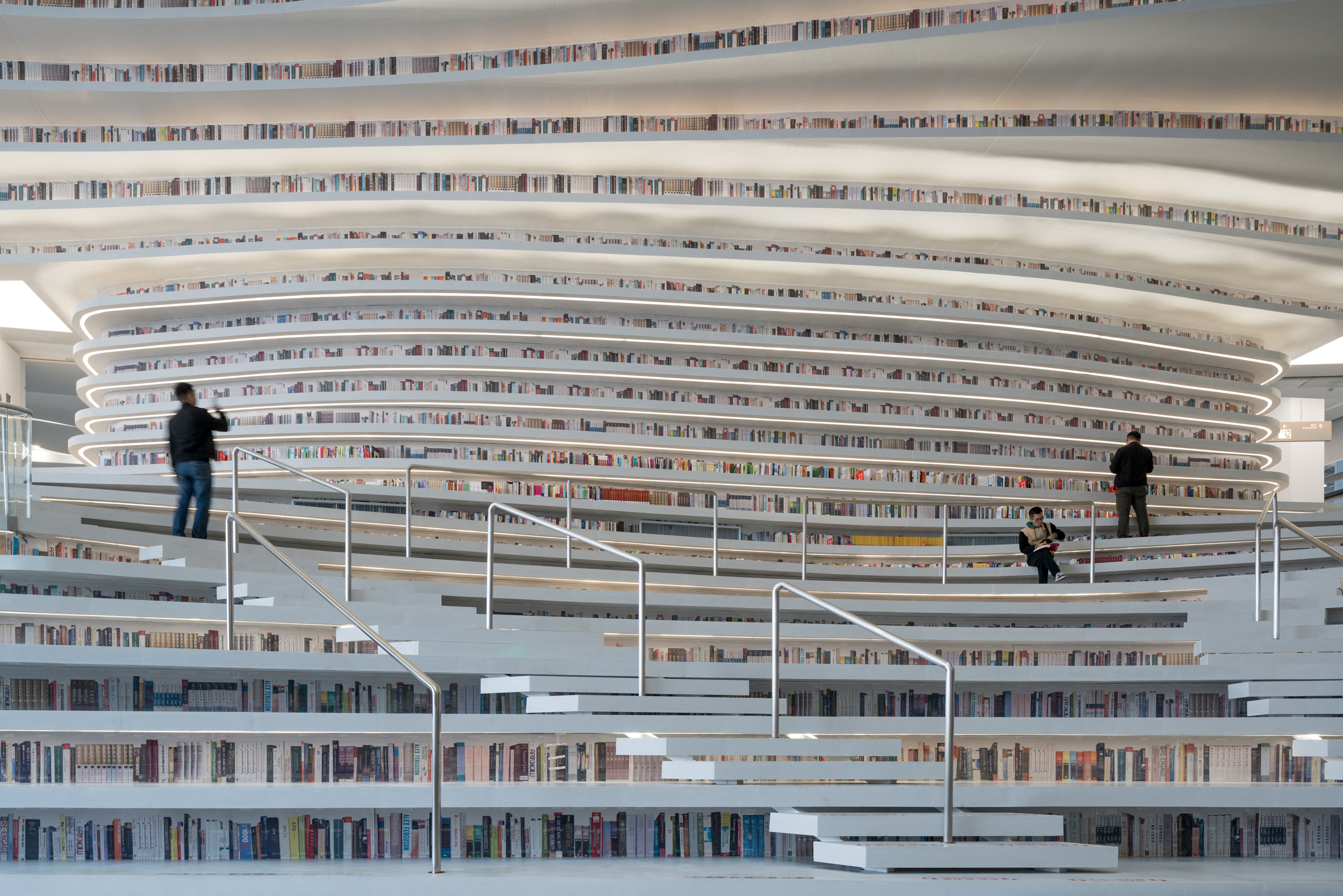 Visitors seated and walking on the terraced Book Mountain inside Tianjin Binhai Library