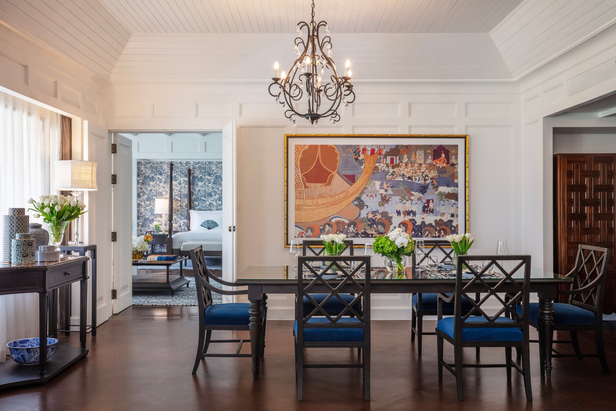 White-panelled dining room of the Jim Thompson suite, with a dark table, blue chairs, and a bedroom beyond