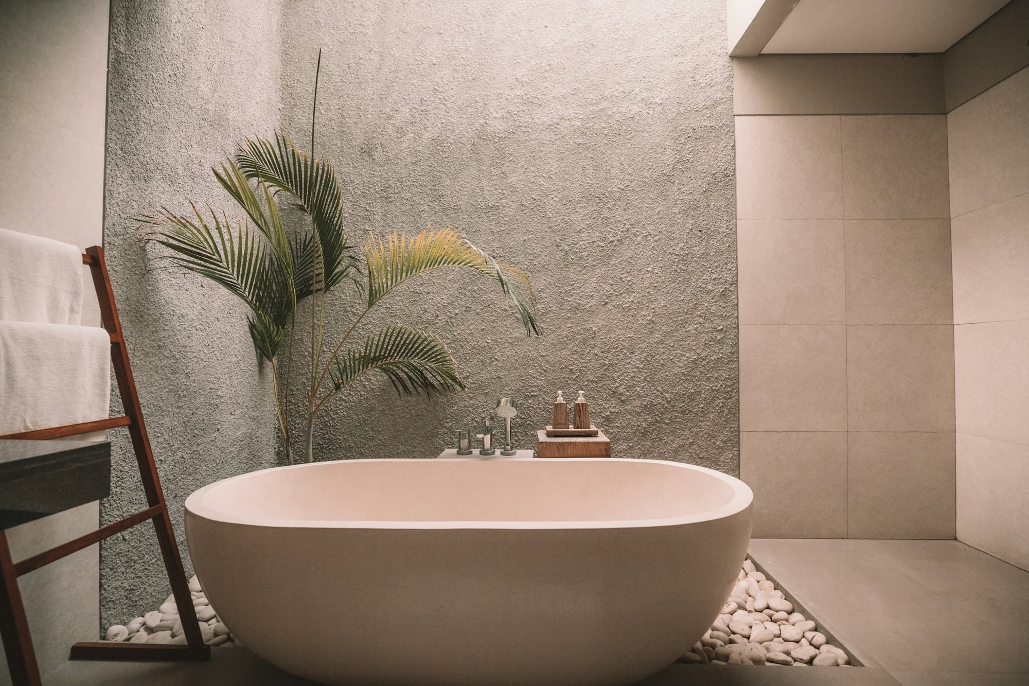 Freestanding bathtub in a stone-lined spa bathroom with folded towels and a palm