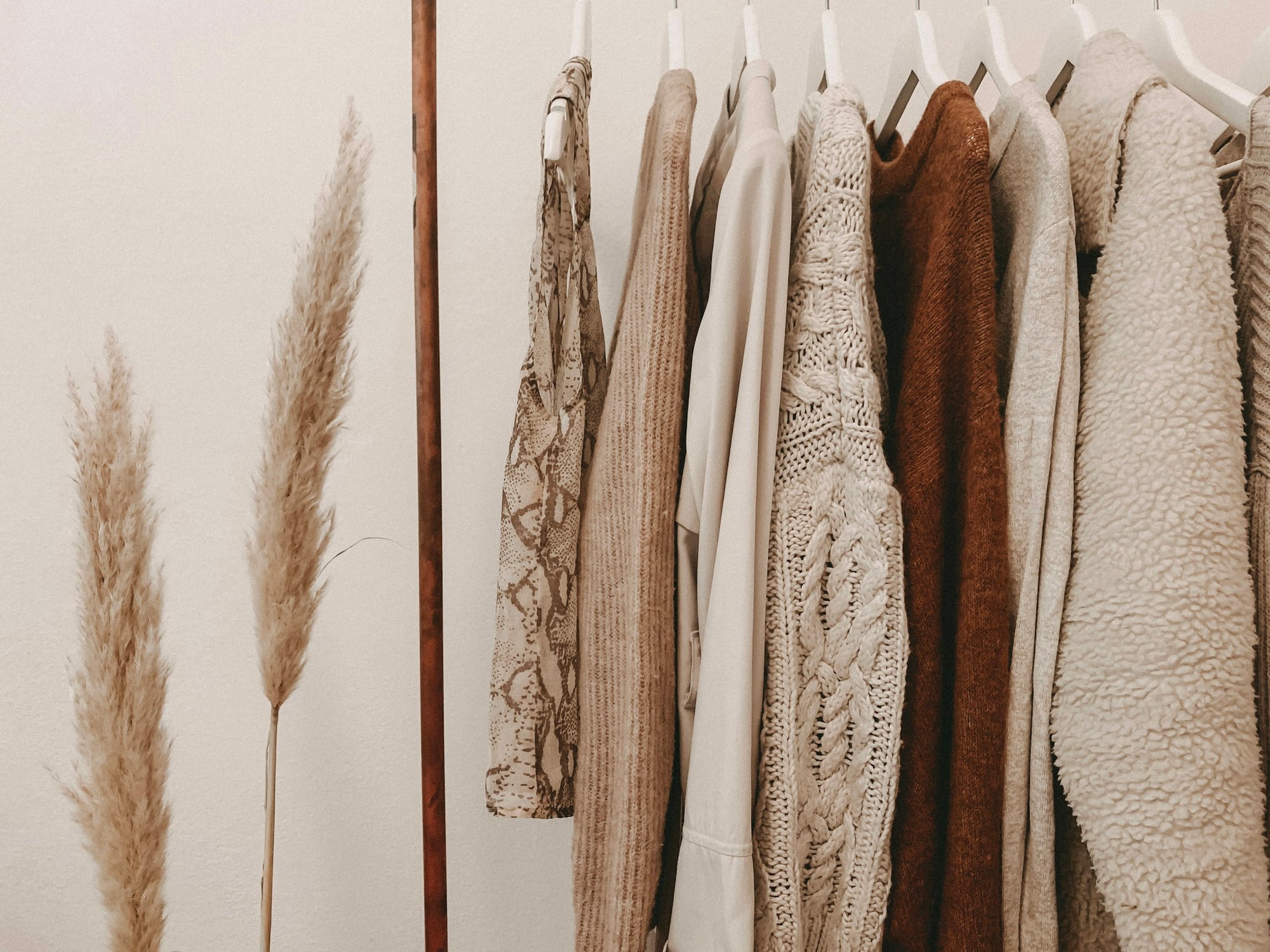 Camel and cream knits and coats hanging on a simple rack with no visible logos