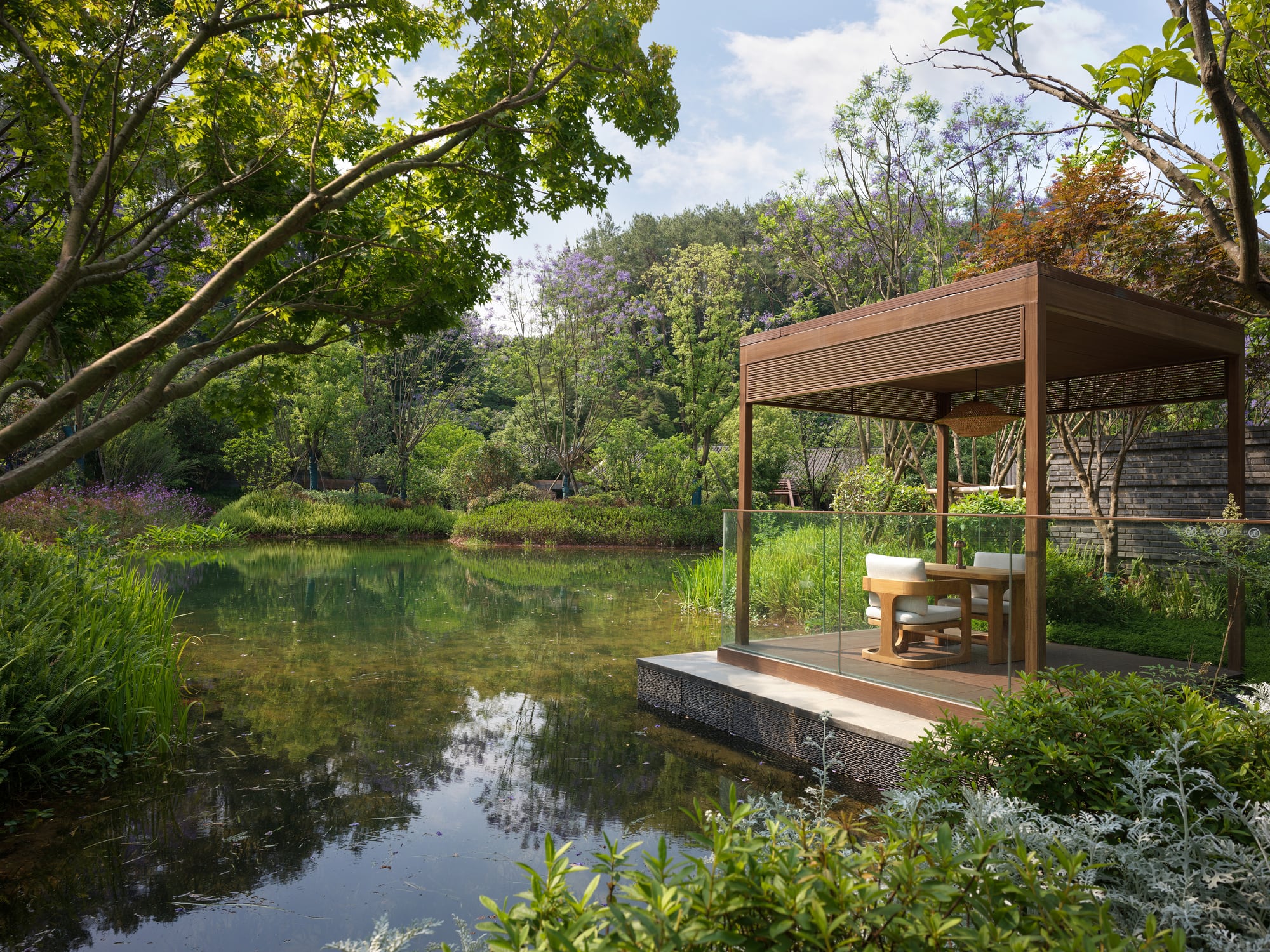 Timber pavilion with two chairs over a still pond at Banyan Tree Mount Emei, Huangwan