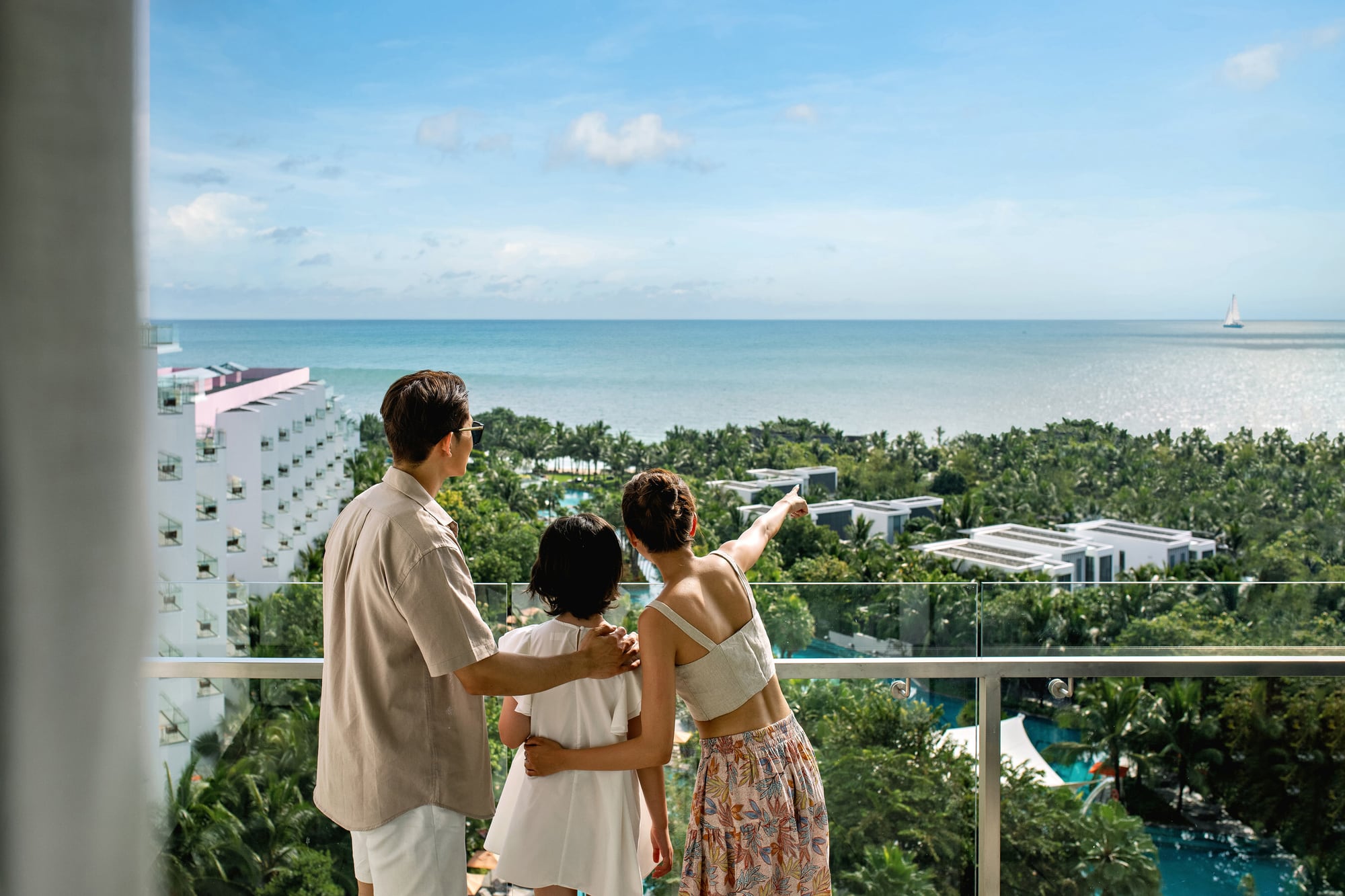 Family on a high balcony at Premier Residences Phu Quoc Emerald Bay overlooking resort roofs and sea