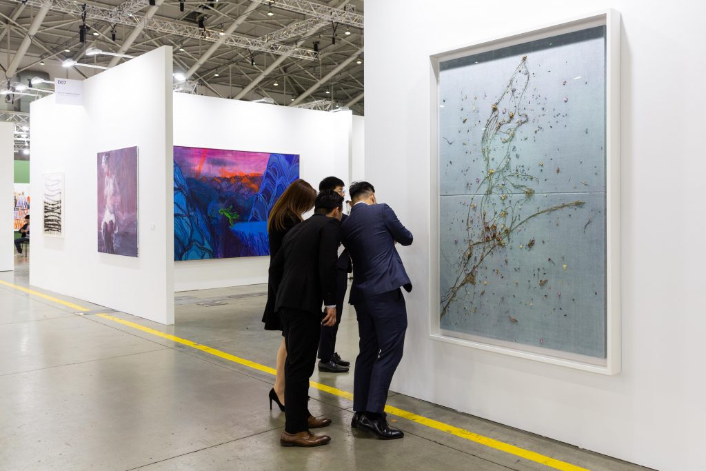 Four visitors studying a large framed work at a Taipei Dangdai gallery booth