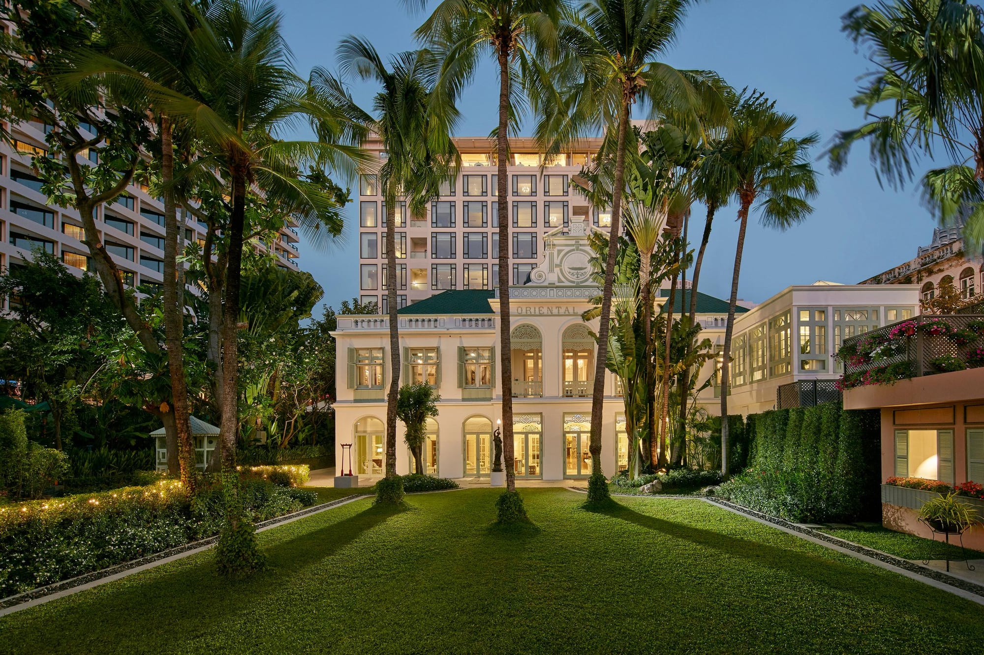 Authors' Wing of Mandarin Oriental Bangkok at dusk with lawn, palms, and white colonial facade